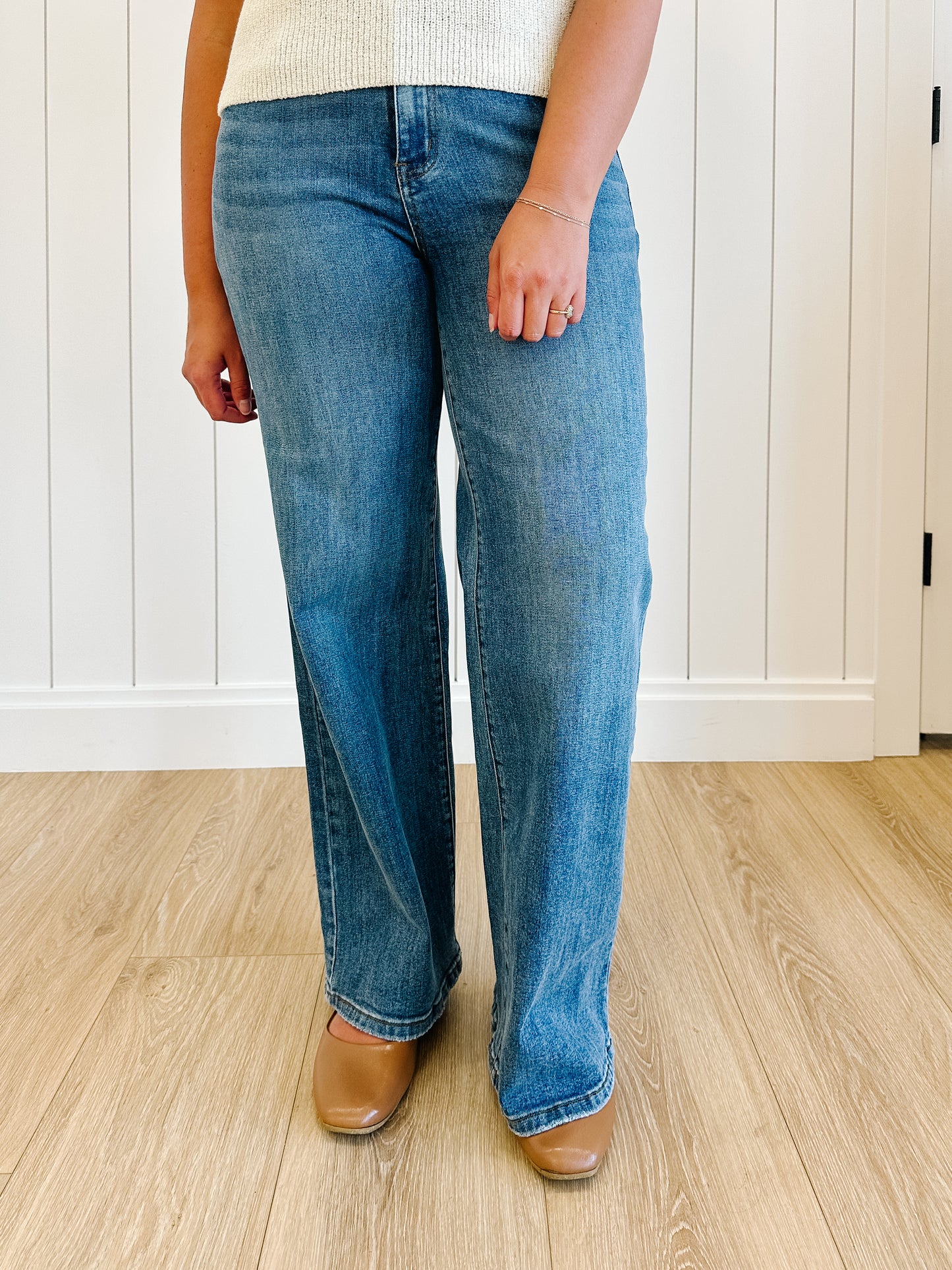 Person wearing blue jeans and brown shoes standing on a wooden floor.