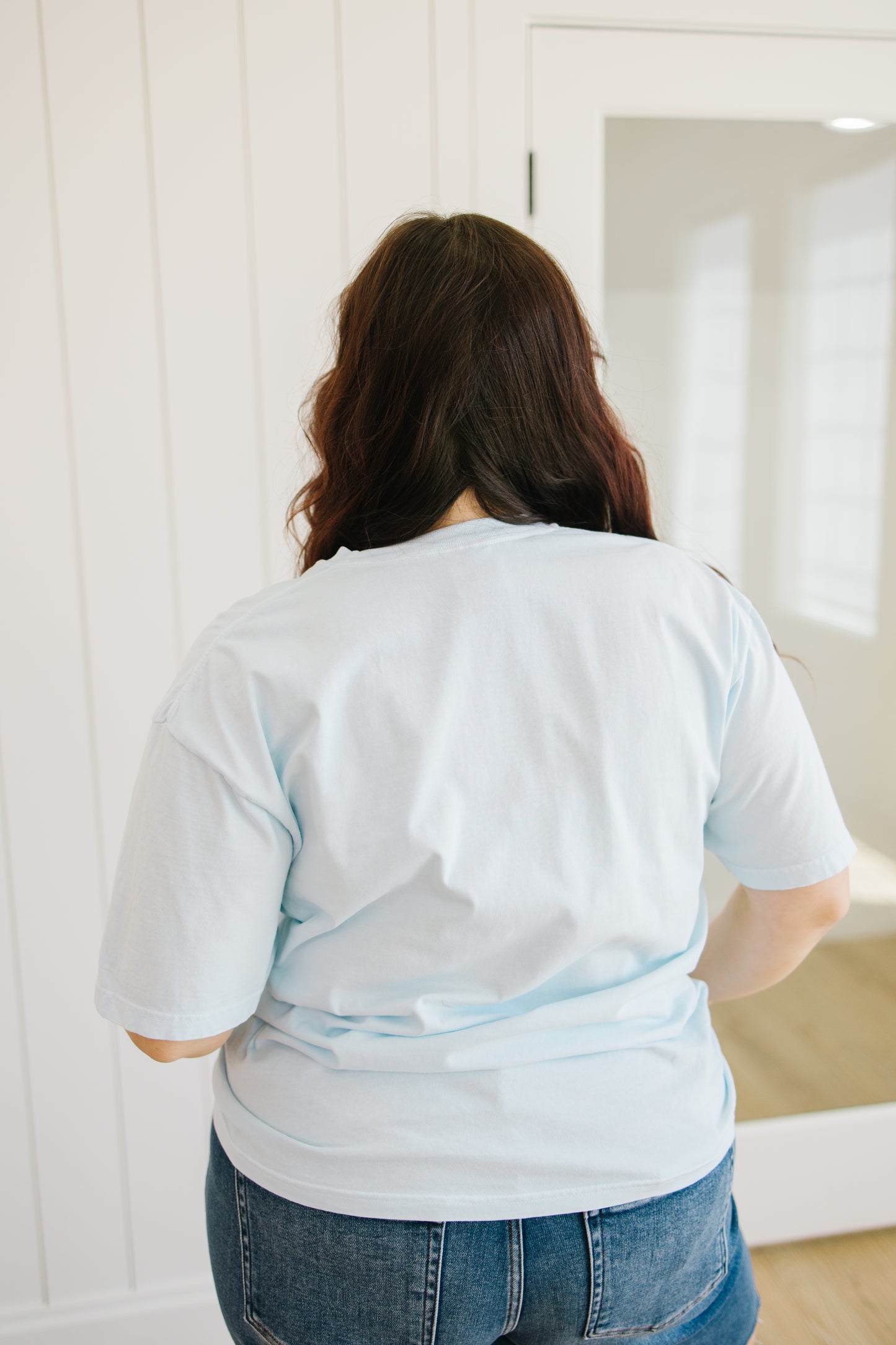 Person wearing a light blue t-shirt and jeans standing in front of a mirror.