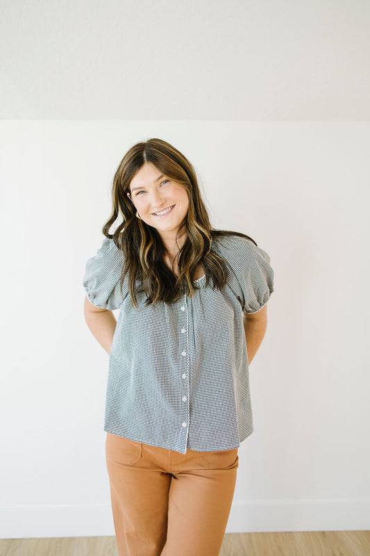 Woman wearing a lblack checkered blouse and brown pants against a white background