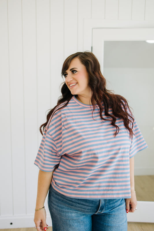 Woman wearing a pink and blue striped shirt and jeans standing in a room with white walls.