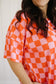 Person wearing a pink and orange checkered dress against a white background