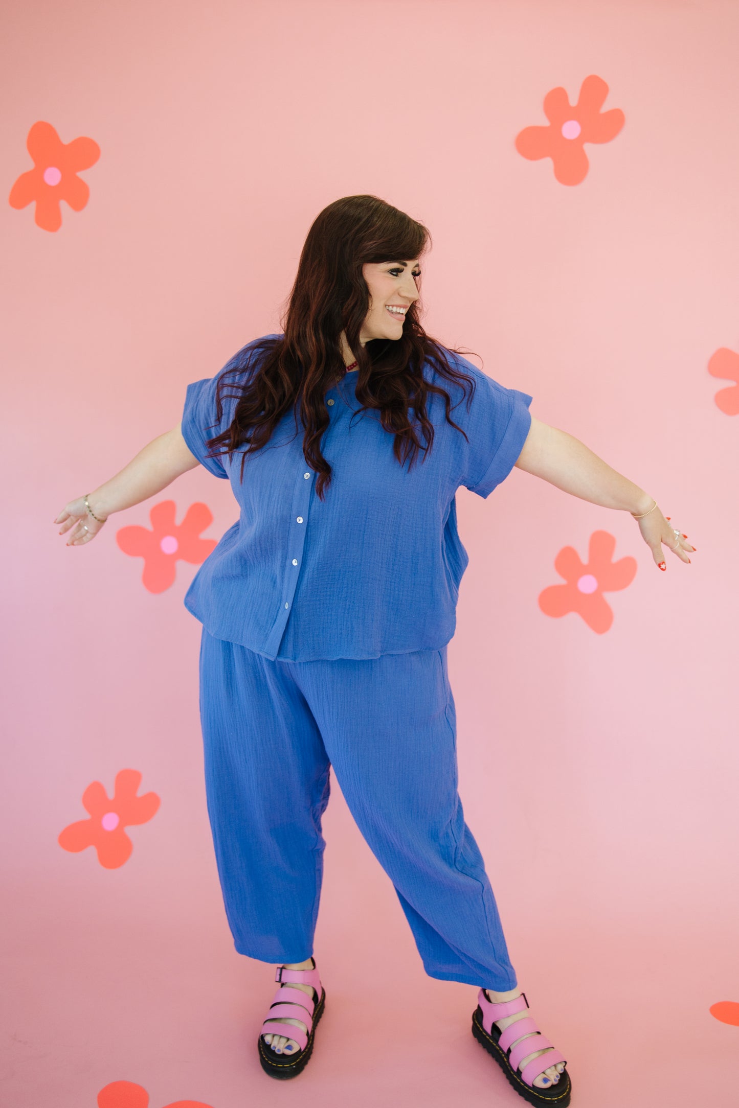 Woman in a blue outfit standing against a pink background with orange flowers