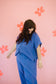 Woman in a blue outfit standing against a pink background with floral patterns