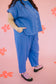 Person wearing a blue outfit with pink sandals on a pink background with flowers.