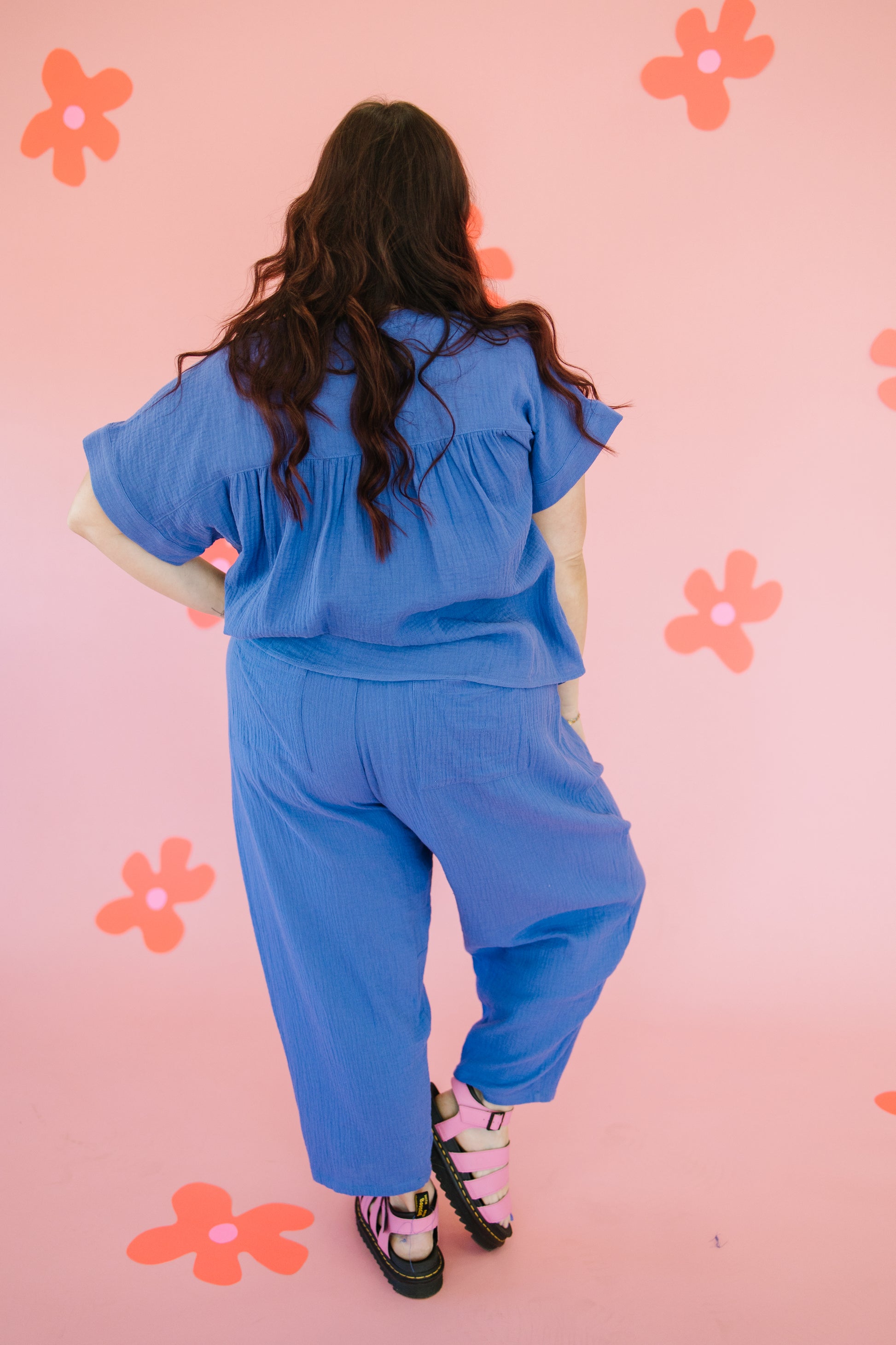 Person wearing a blue outfit standing against a pink background with flower patterns