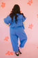 Person wearing a blue outfit standing against a pink background with flower patterns