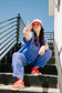 Person in blue jumpsuit and red sneakers making a peace sign on black steps with clear blue sky.