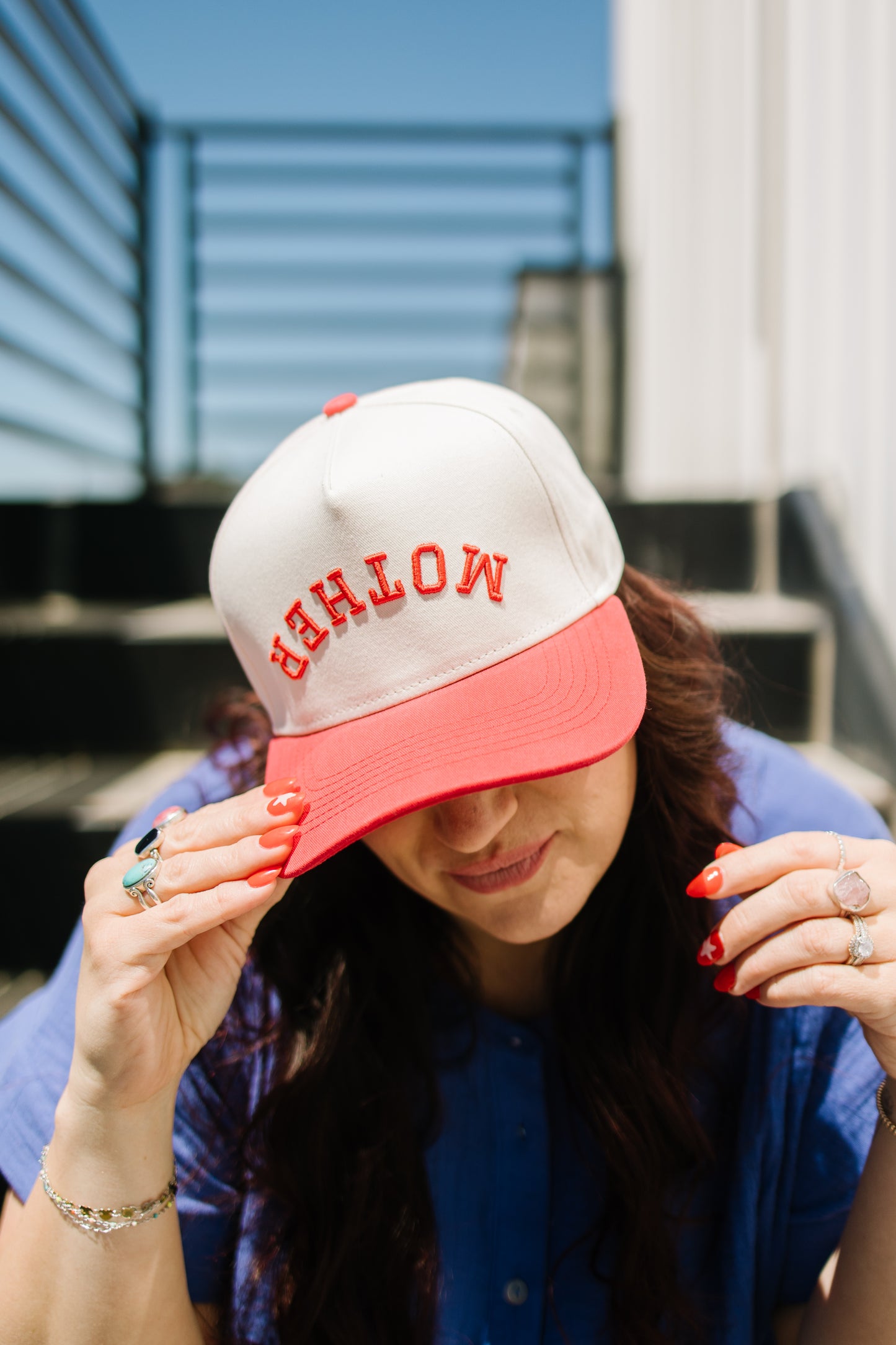 Person wearing a cap with 'mother' text, sitting outdoors.