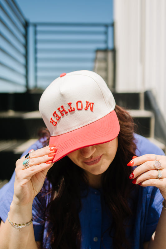 Person wearing a cap with 'mother' text, sitting outdoors.