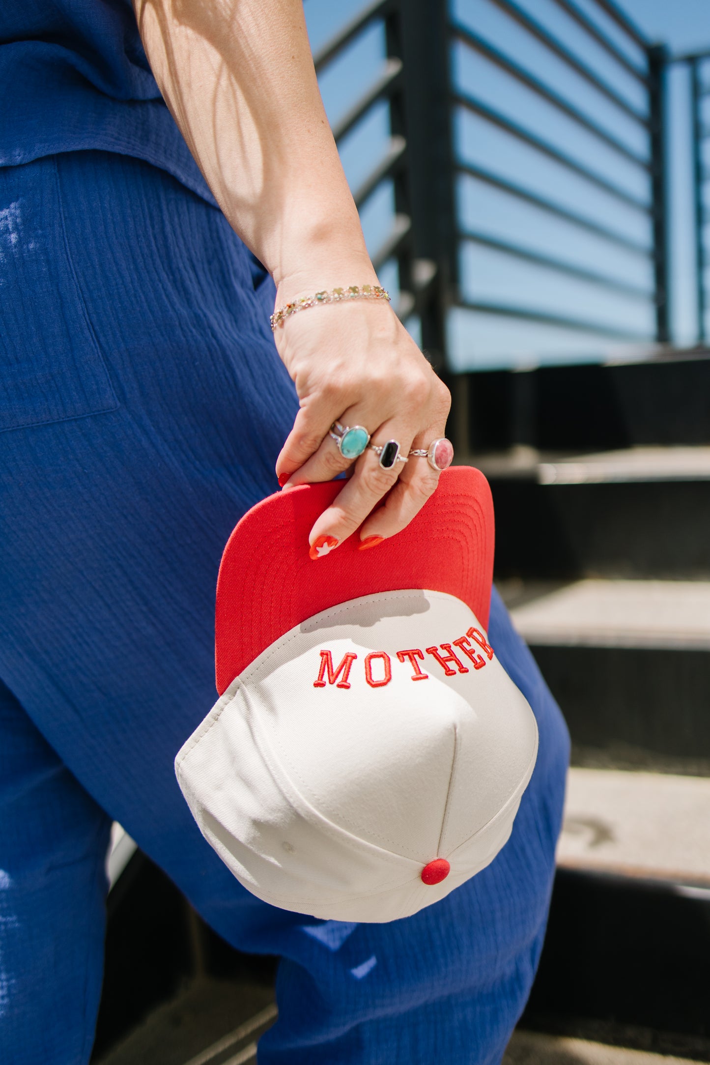 Person holding a red and white cap with 'MOTHER' printed on it, wearing a blue outfit.