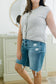 Woman wearing a gray sleeveless top and blue denim shorts in a room.