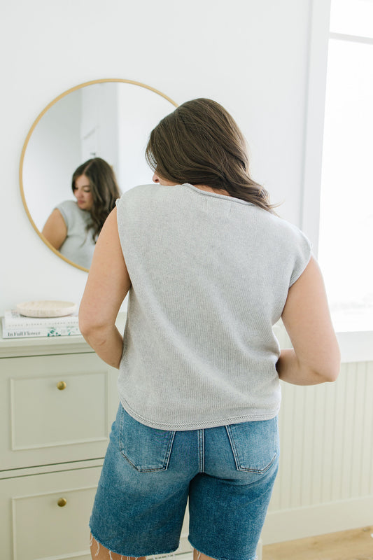 Woman wearing a gray t-shirt and blue shorts standing in front of a mirror.