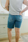 Person wearing blue denim shorts and a gray top in a room with a dresser and window.