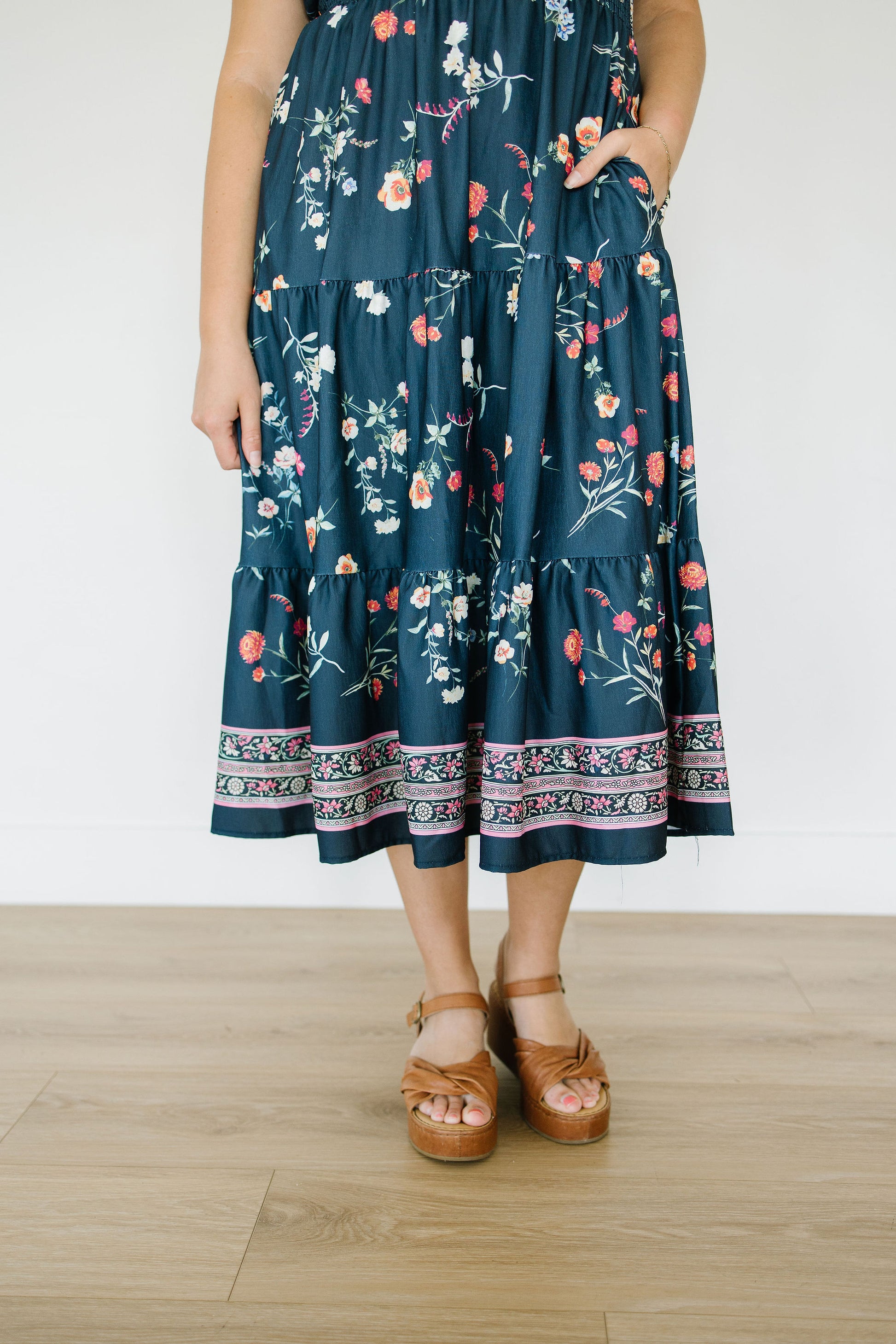 Person wearing a dark blue floral dress on a light wooden floor.