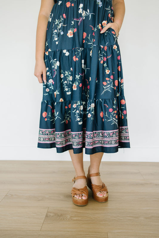 Person wearing a dark blue floral dress on a light wooden floor.