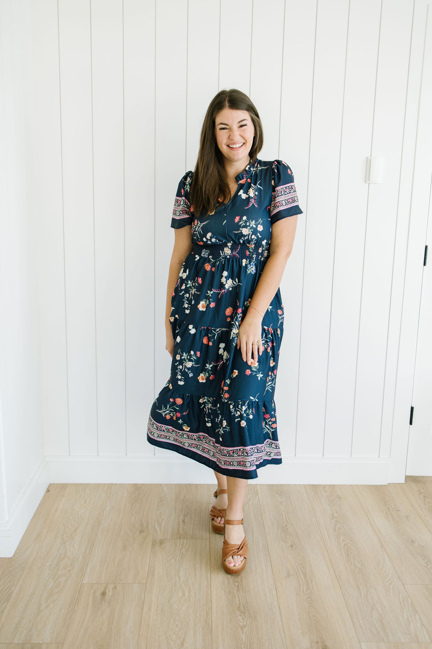Woman wearing a navy floral dress standing against a white paneled wall.