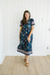 Woman wearing a navy floral dress standing against a white paneled wall.