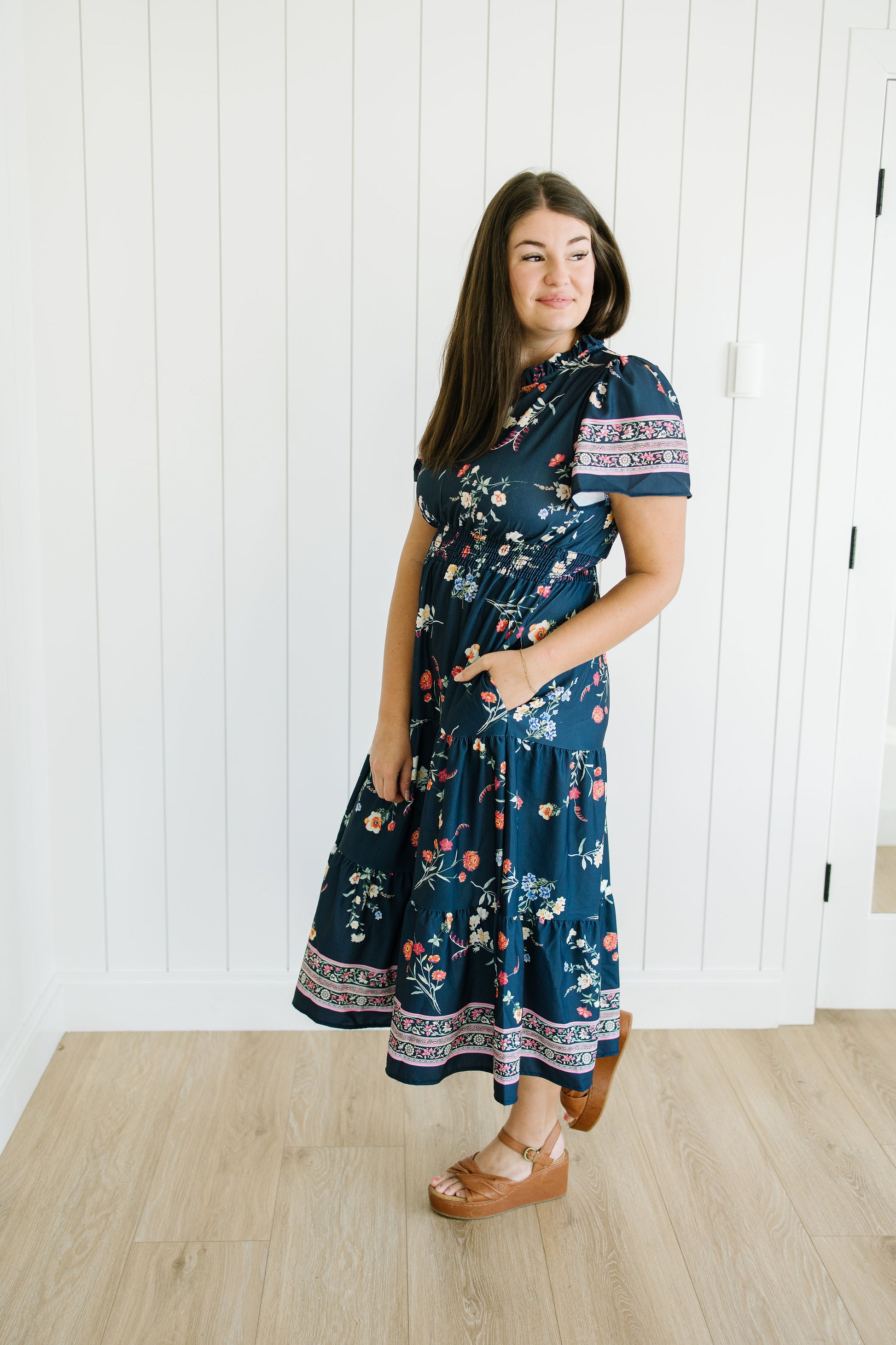 Woman wearing a blue floral dress standing in a room with white paneled walls.