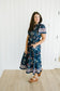 Woman wearing a blue floral dress standing in a room with white paneled walls.
