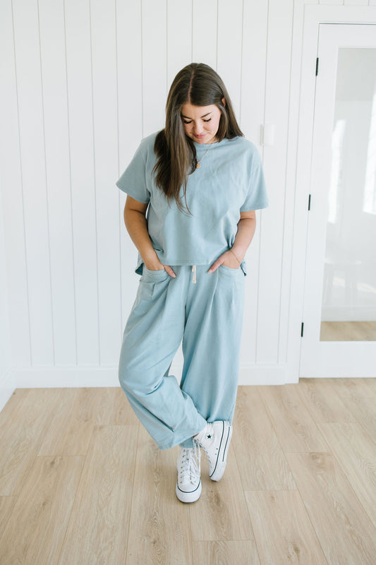Woman wearing a light blue outfit standing in a room with white walls and wooden floor.
