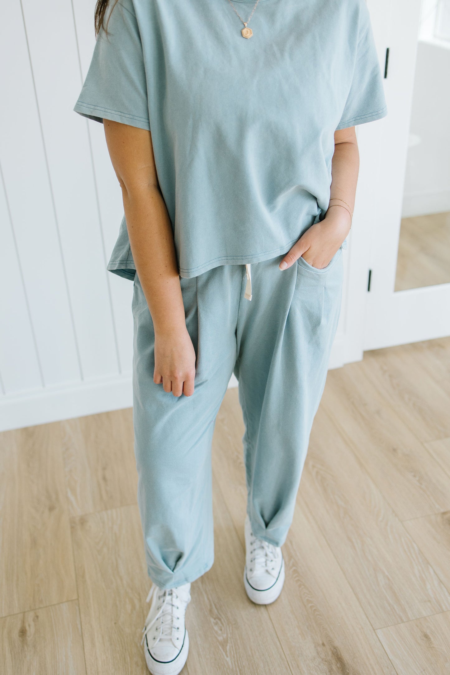 Person wearing a light blue outfit with white sneakers in a minimal indoor setting
