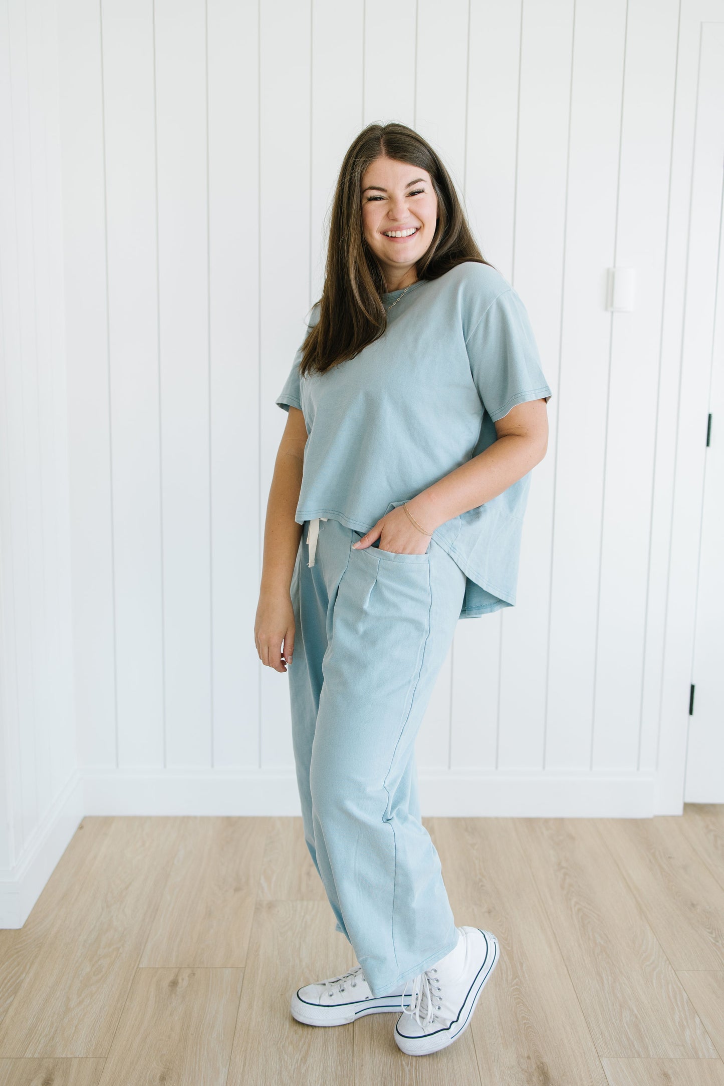 Woman wearing a light blue outfit standing against a white wall.