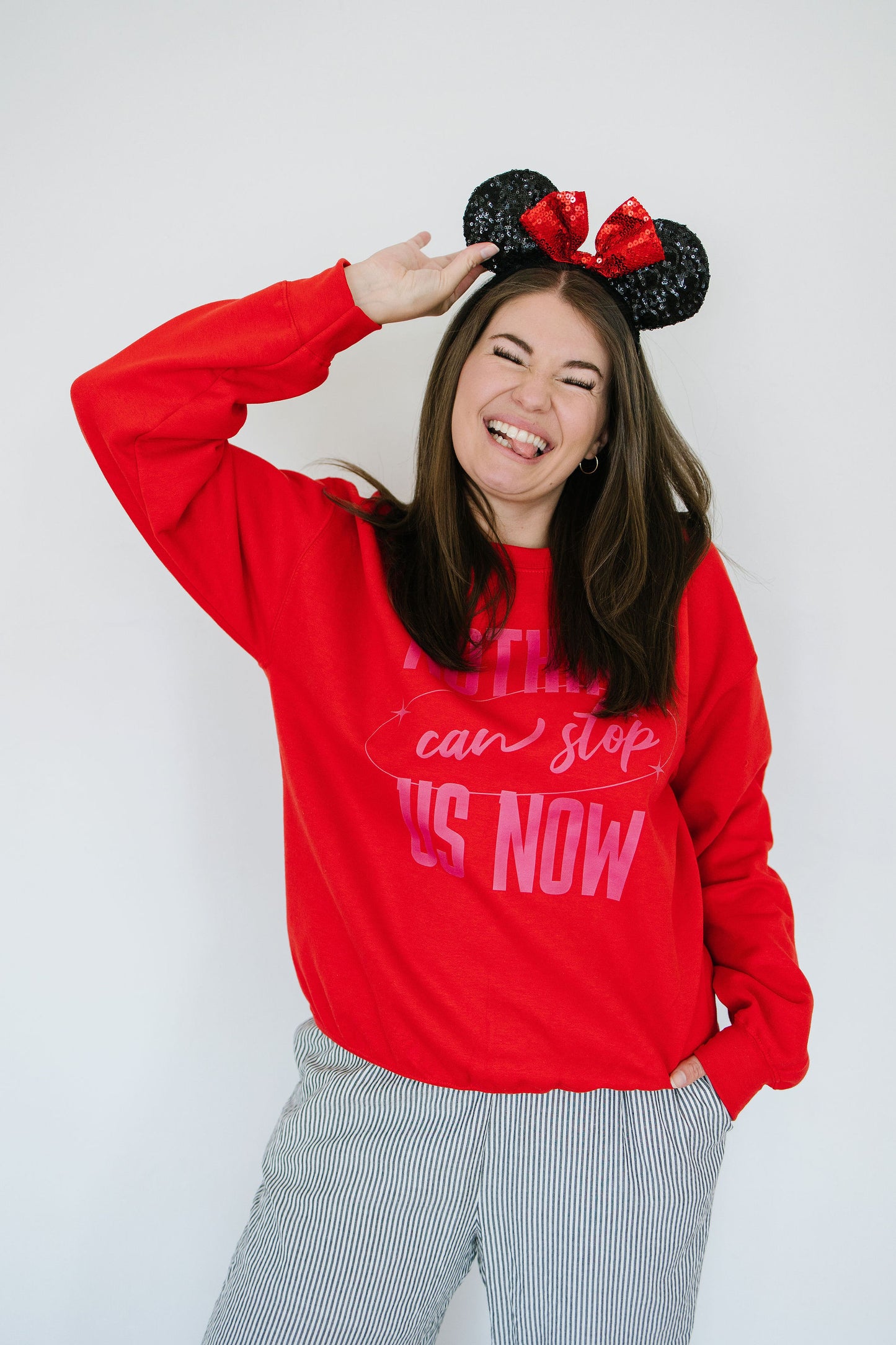 Person wearing a red sweatshirt with text and black mouse ears with red bows on a white background
