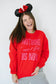 Person wearing a red sweatshirt with pink text and Minnie Mouse ears against a white background