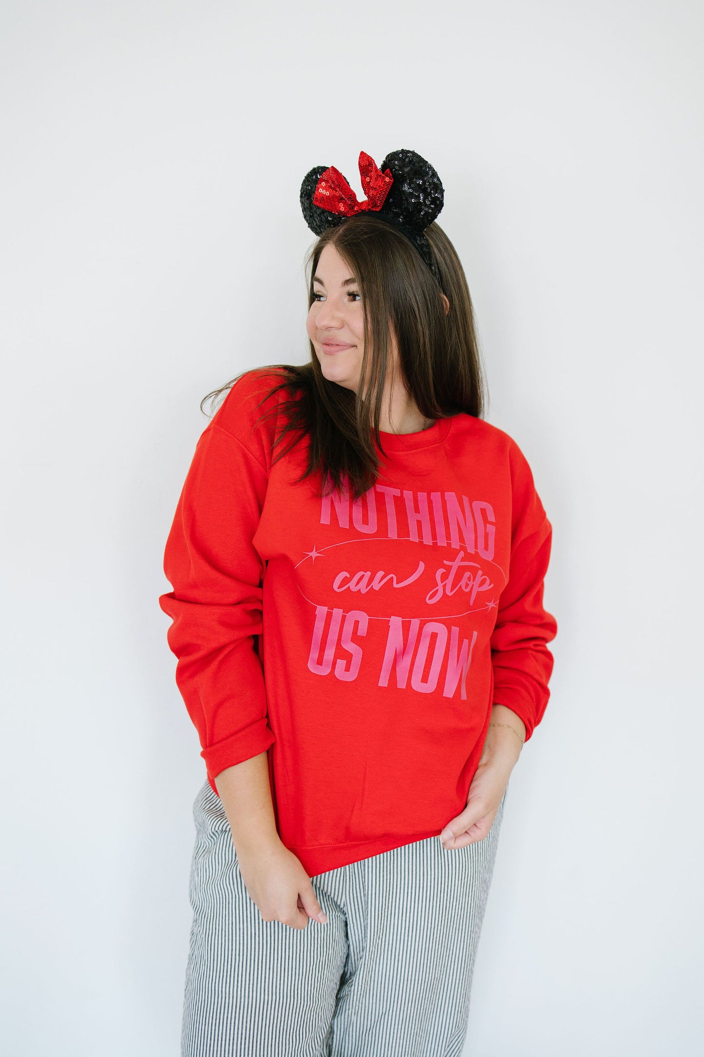 Person wearing a red sweatshirt with text and Minnie Mouse ears on a plain background
