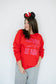 Person wearing a red sweatshirt with text and Minnie Mouse ears on a plain background