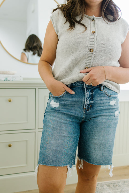 Person wearing a beige sleeveless top and blue denim shorts in a bathroom setting.