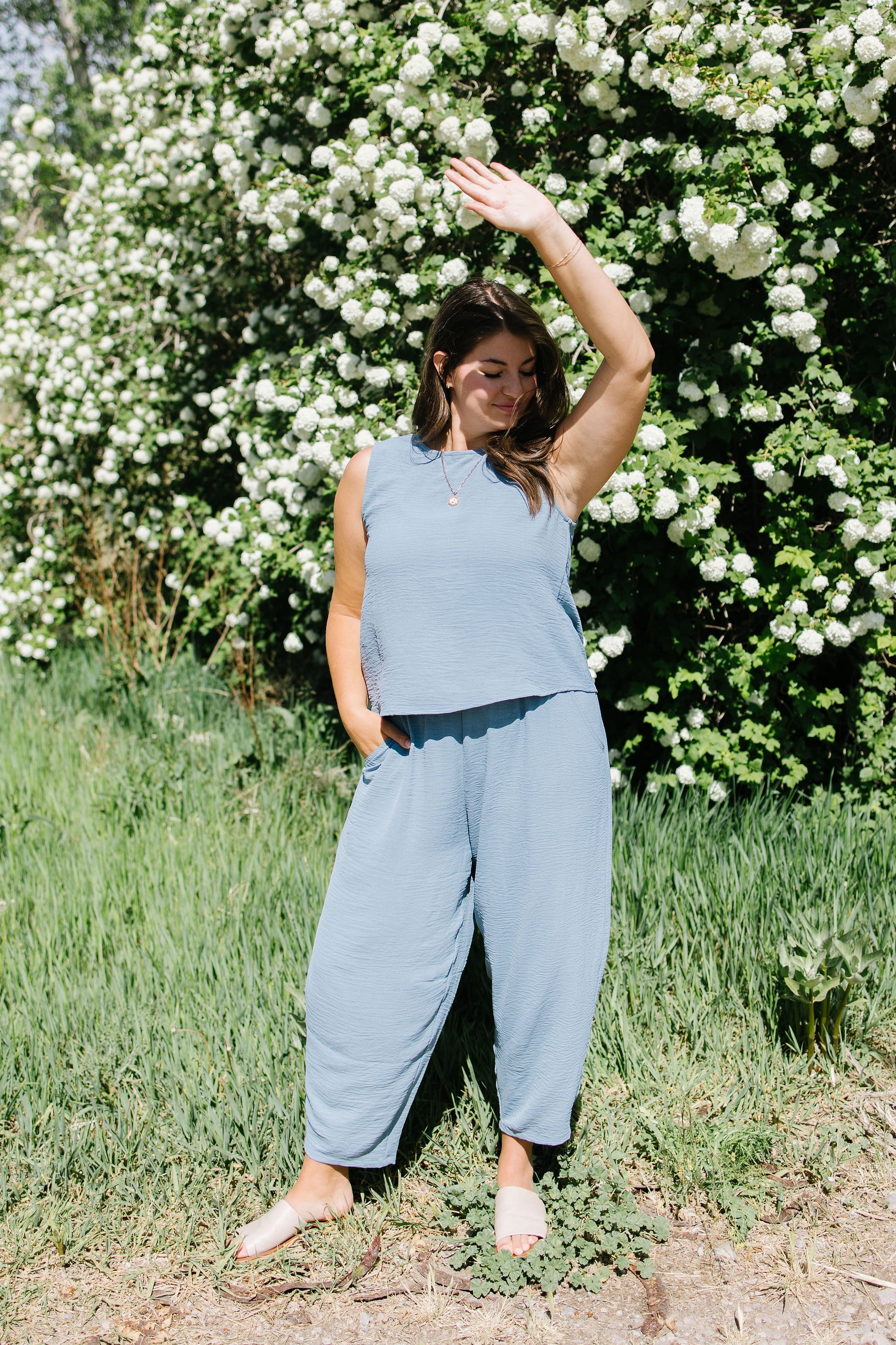 Woman in a light blue outfit standing in front of a white flower bush