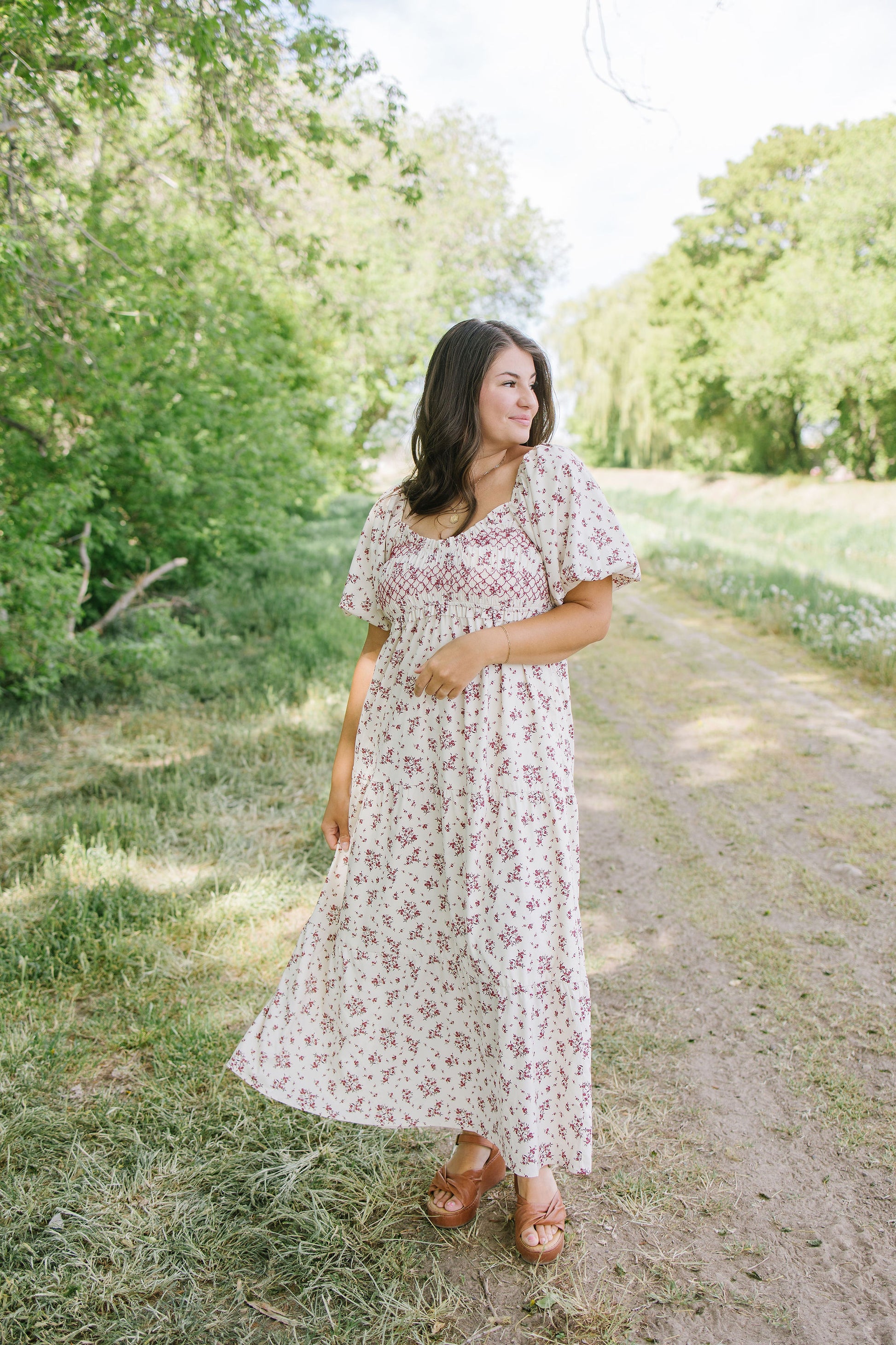 Woman in a floral dress standing on a dirt path with trees in the background