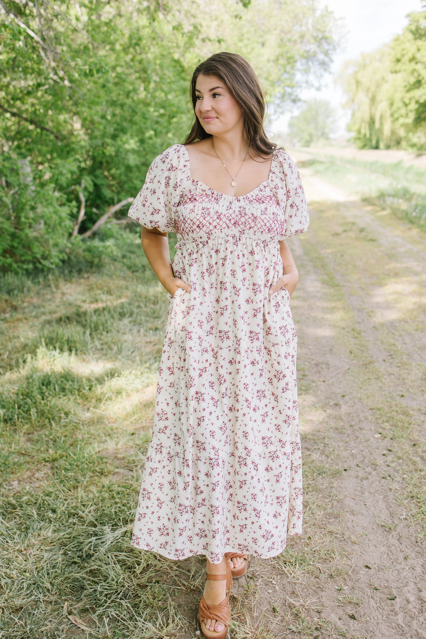 Woman in a floral dress standing on a dirt path with trees in the background