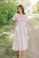 Woman in a floral dress standing on a dirt path with trees in the background