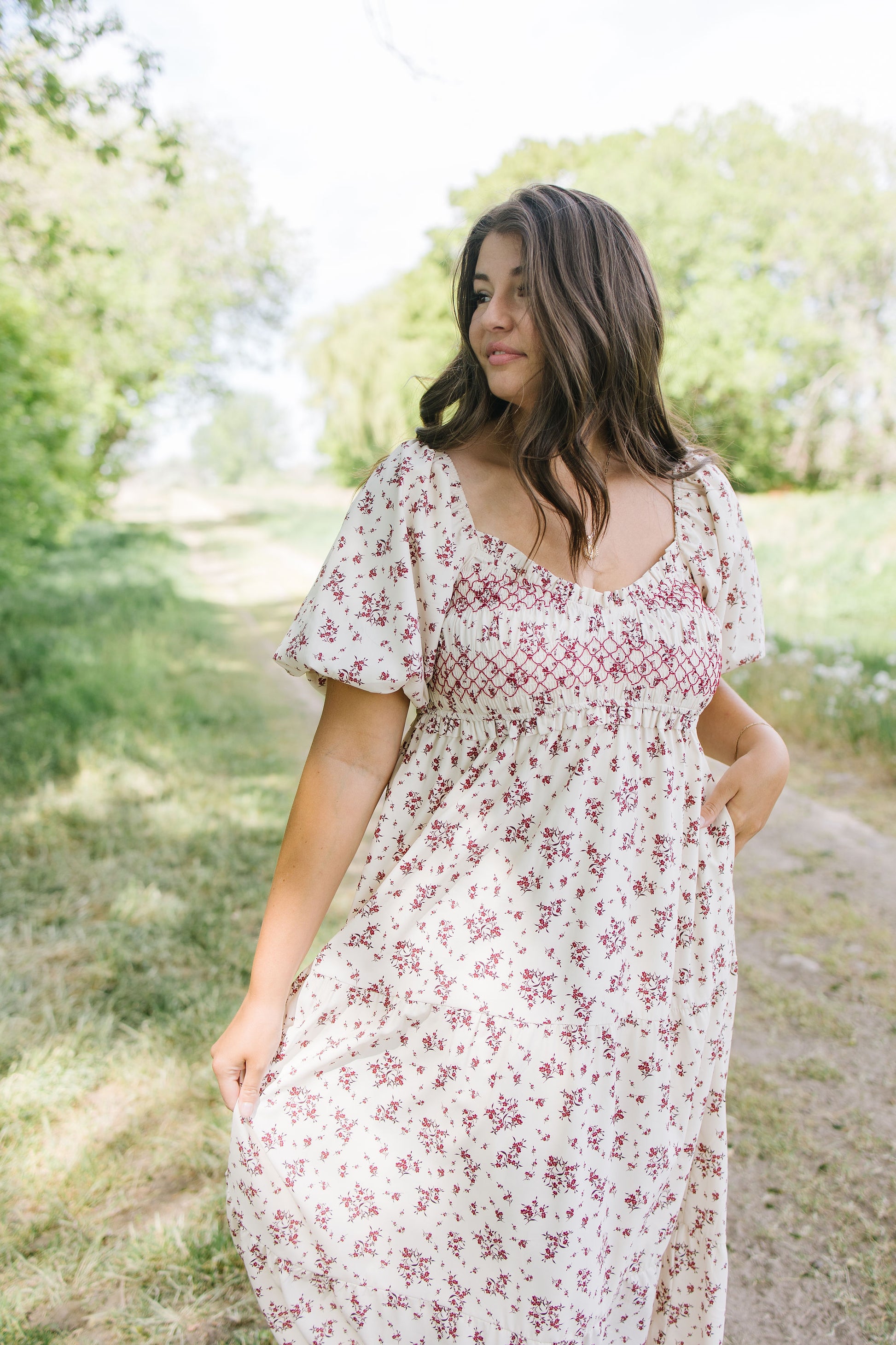 Woman wearing a floral dress standing outdoors with greenery in the background