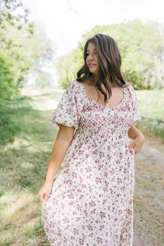 Woman wearing a floral dress standing outdoors with greenery in the background