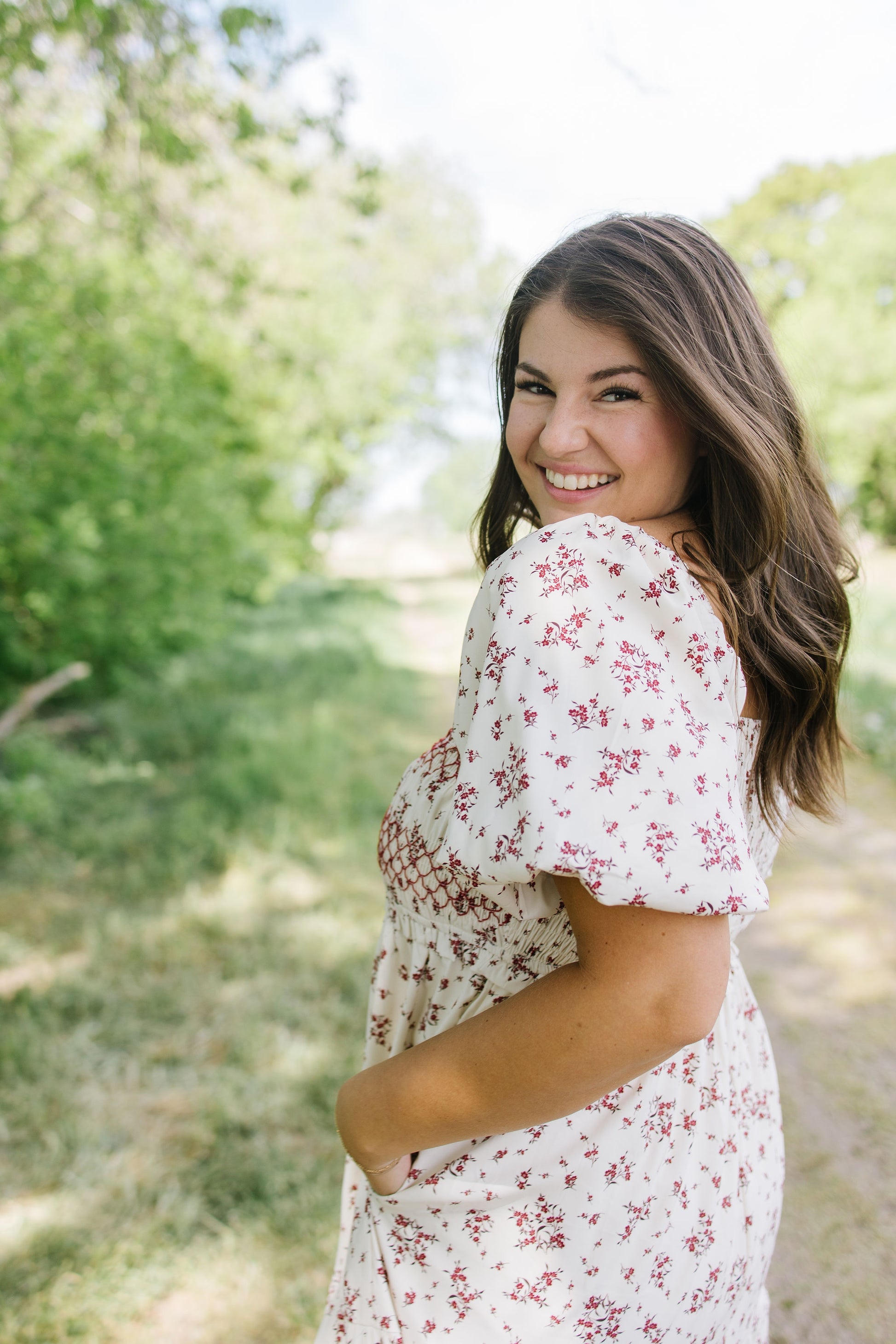 Woman in a floral dress standing outdoors with greenery in the background