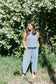 Woman in a blue set standing in front of a white flower bush