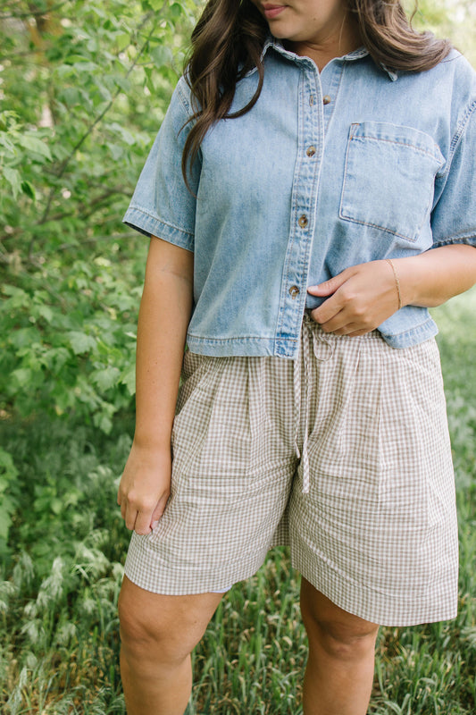Person wearing a denim shirt and plaid shorts standing in a natural setting
