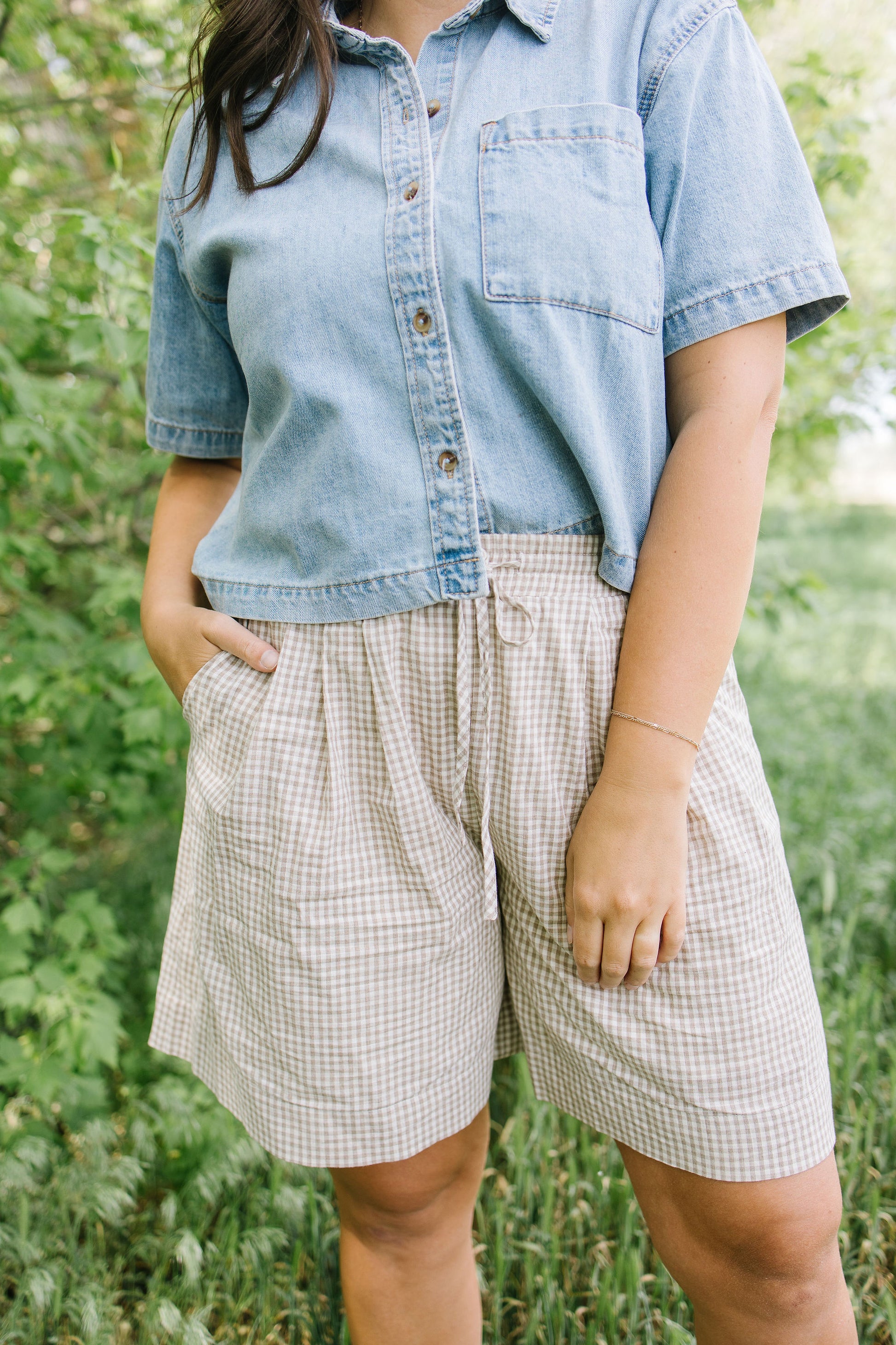 Person wearing a denim shirt and checkered shorts standing in a natural setting
