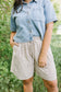 Person wearing a denim shirt and checkered shorts standing in a natural setting