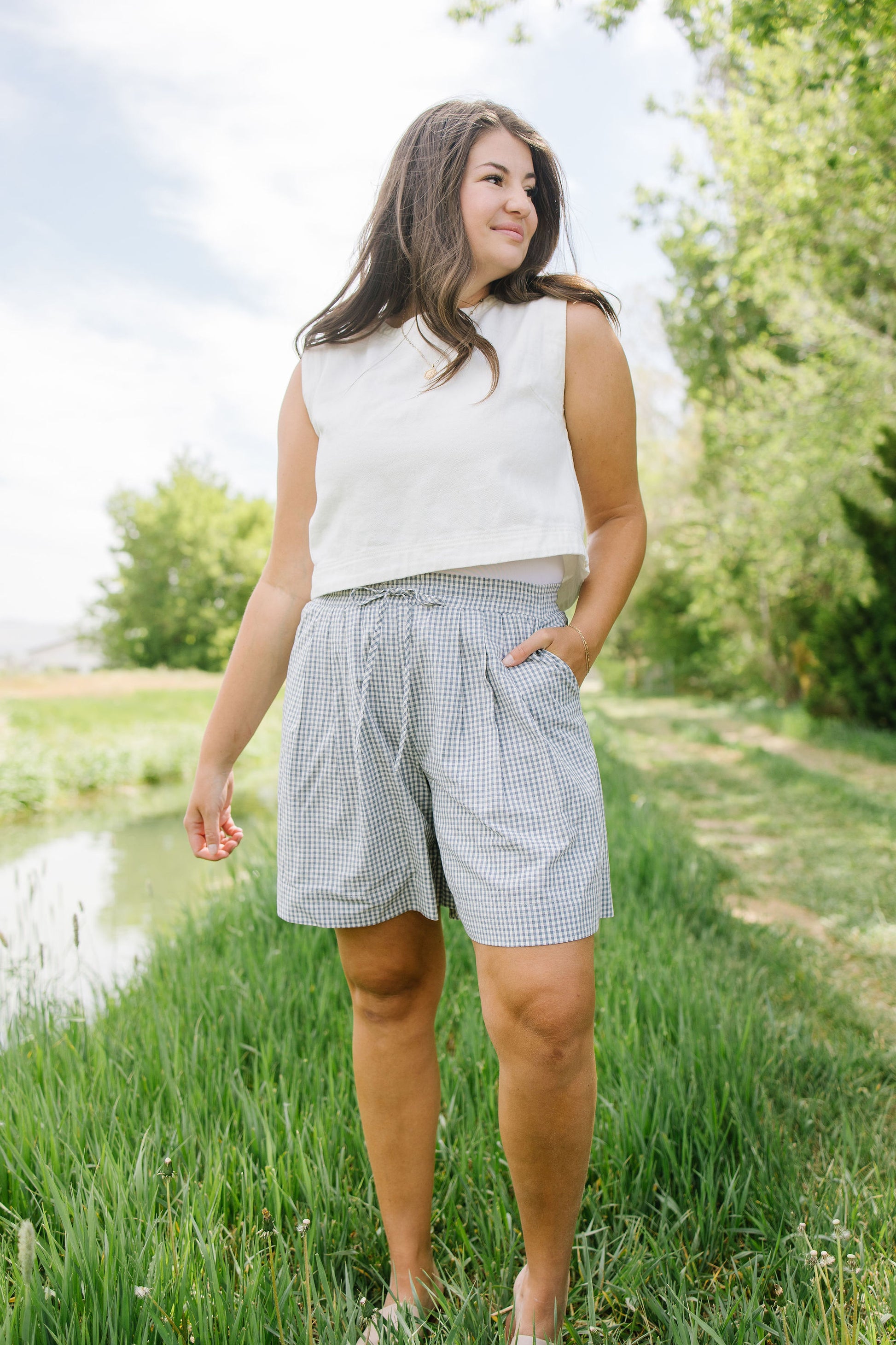Woman standing in a grassy area with trees and a pond in the background