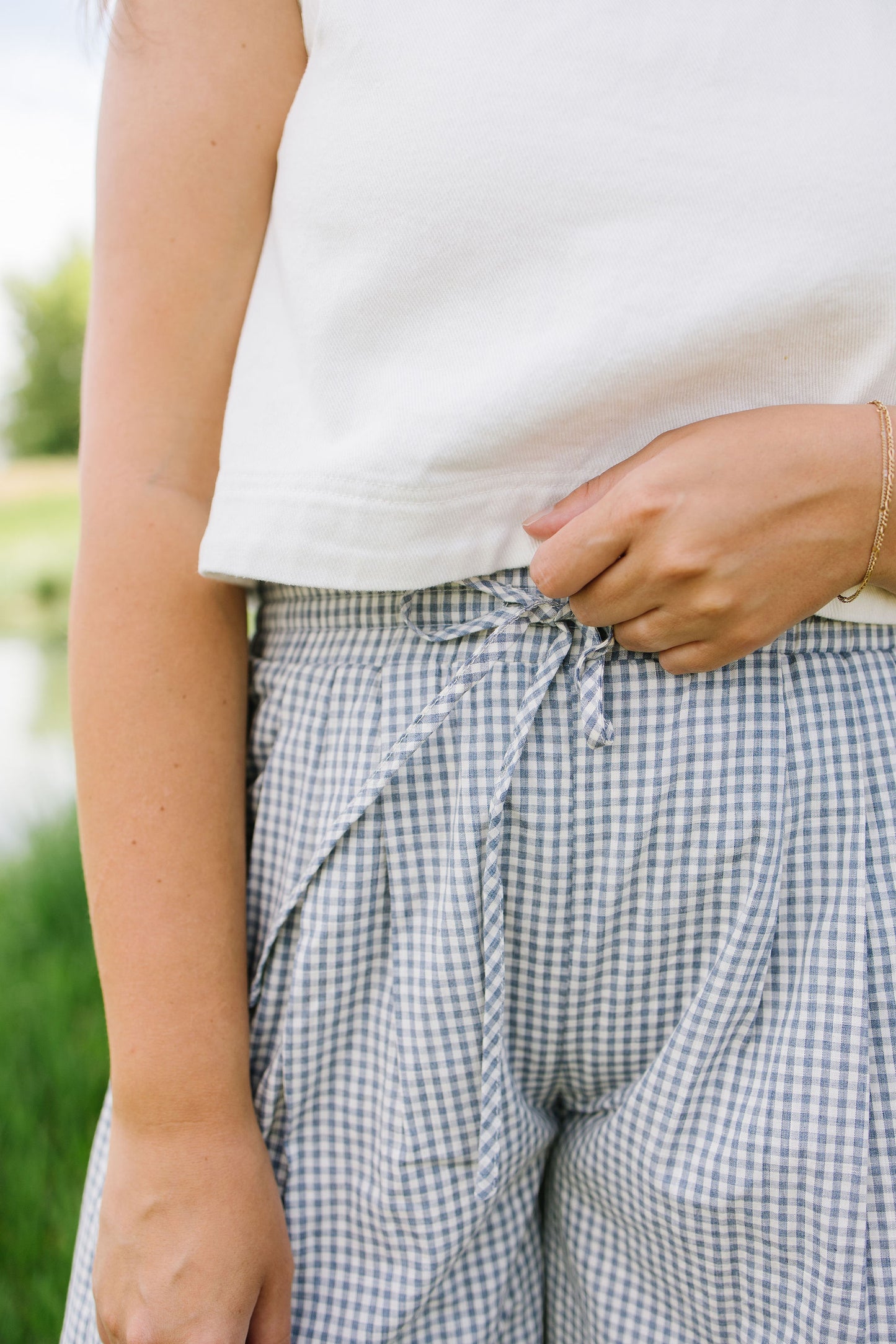 Person wearing a white top and checkered pants with a blurred green background