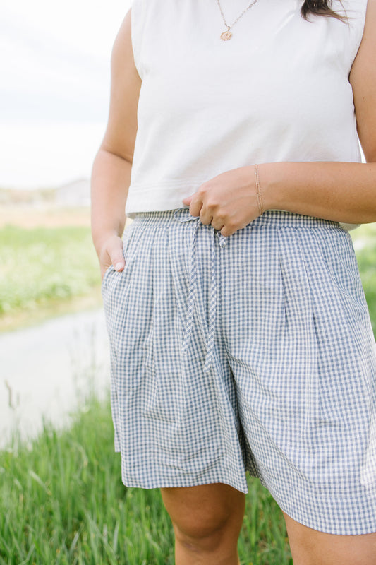 Person wearing a white sleeveless top and checkered shorts in an outdoor setting
