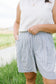 Person wearing a white sleeveless top and checkered shorts in an outdoor setting