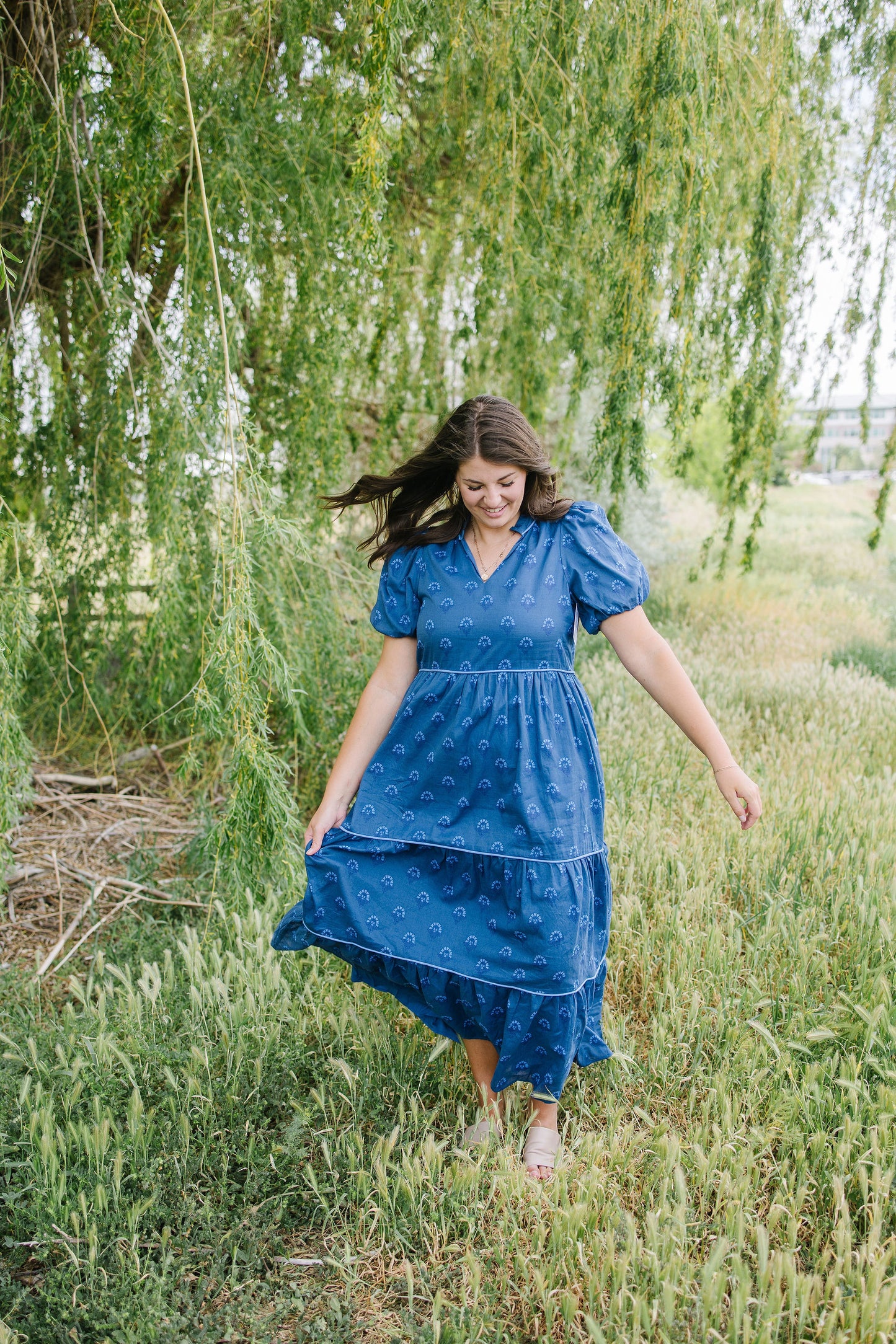 Woman in a blue dress standing in a field with trees in the background