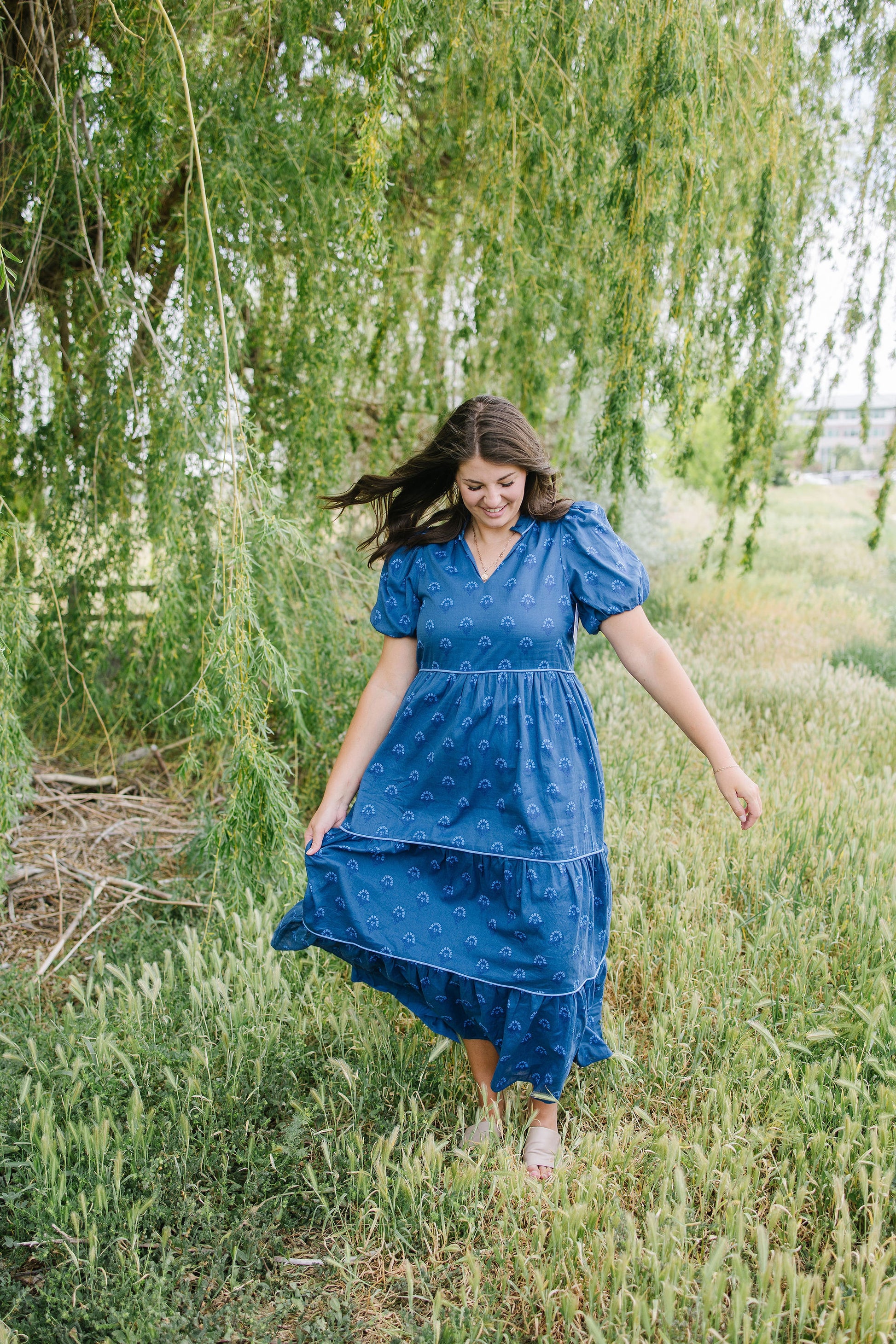 Woman in a blue dress standing in a field with trees in the background