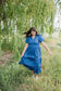 Woman in a blue dress standing in a field with trees in the background