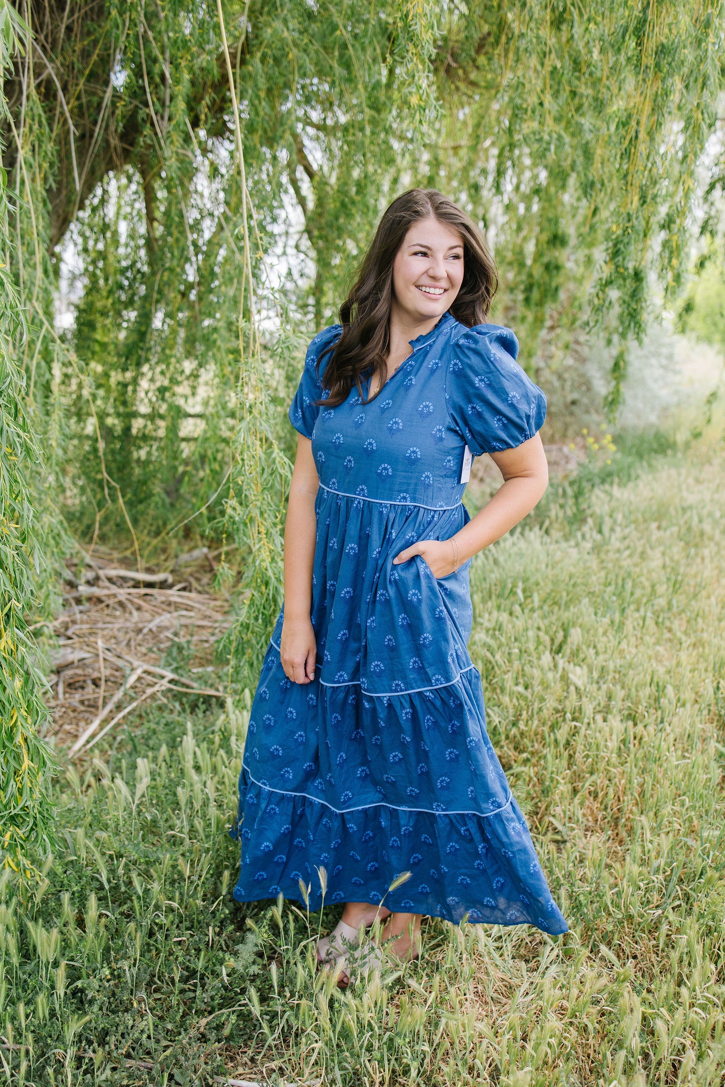 Woman in a blue dress standing in a field with greenery around